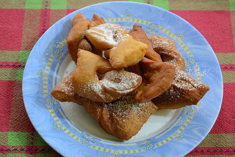 Calzones rotos - fried dough that is knotted and sprinkled with powdered sugar, sitting on a plate.